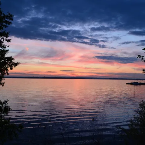 Stiller Sonnenuntergang über einem See in warmem Rosa-Orange, gespiegelt auf ruhigem Wasser