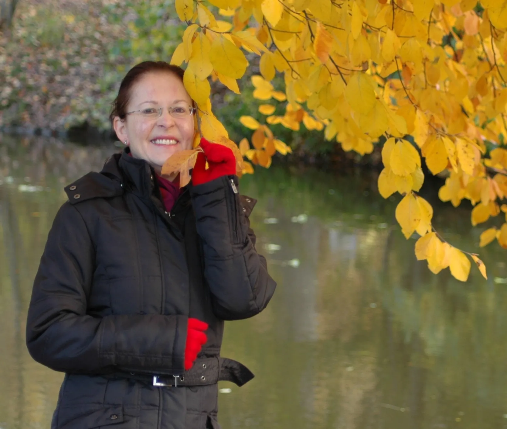 Martina Meyer steht lächelnd am Wasser unter goldgelbem Herbstlaub